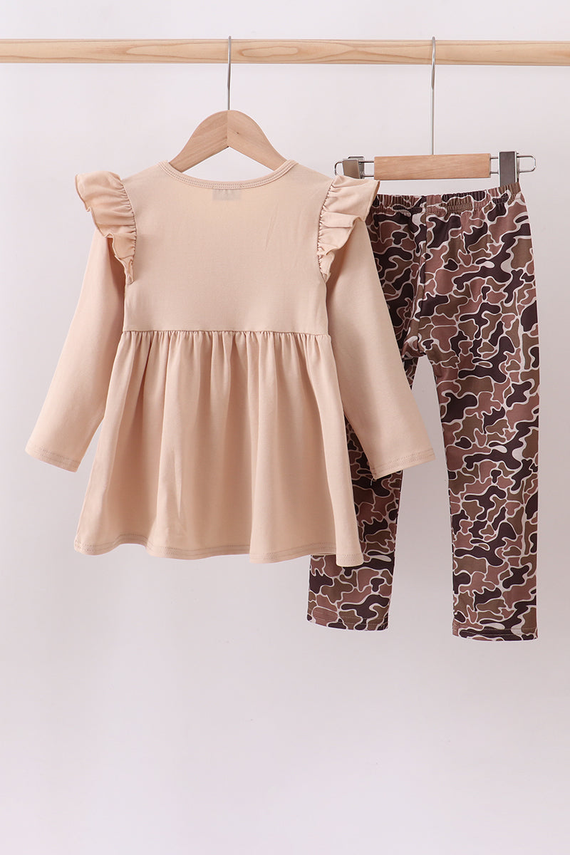 Beige dress and patterned leggings on hangers against a white background