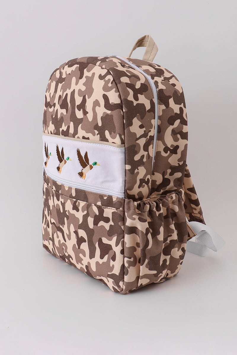 Camouflage-patterned backpack with a white patch featuring a design on a light gray background