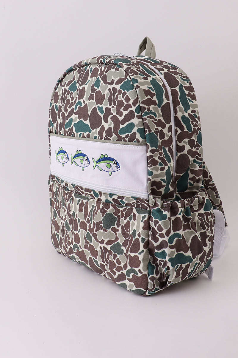 Backpack with camouflage pattern and white patch with fish design on a light gray background