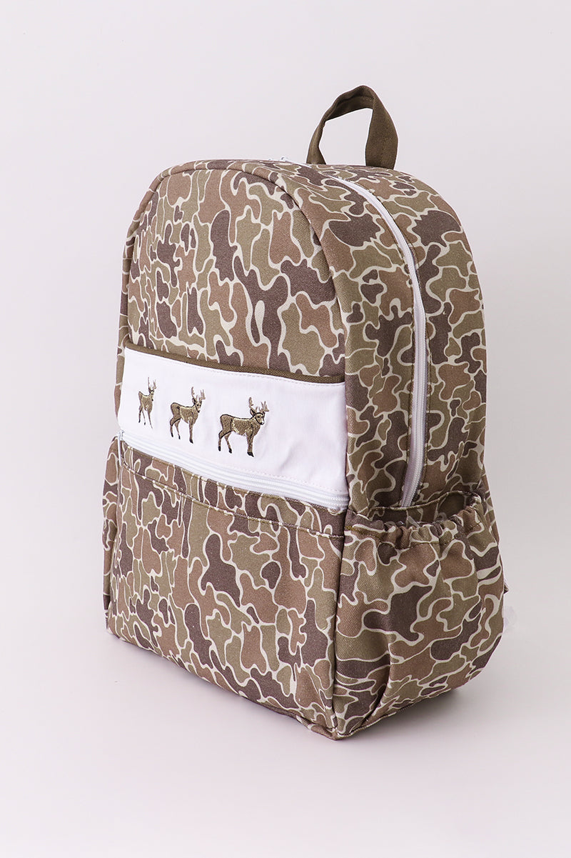 Camouflage-patterned backpack with a white patch featuring deer illustrations on a light gray background