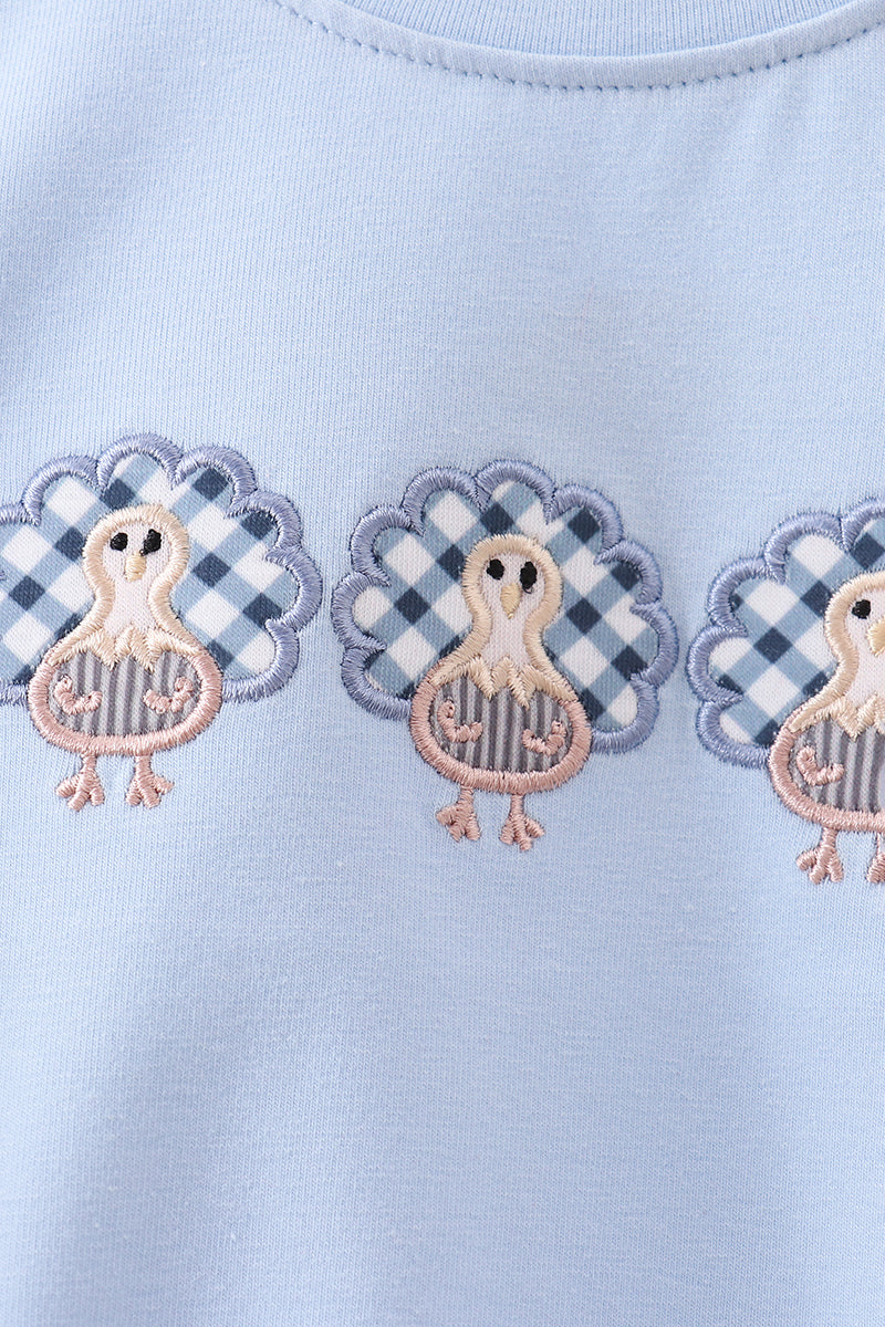 Light blue fabric with embroidered turkey designs on a checkered background