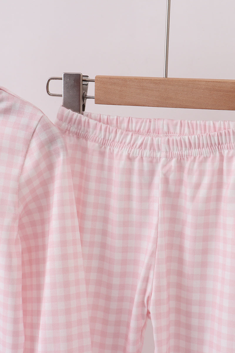 Pink checkered pants hanging on a wooden hanger against a light background