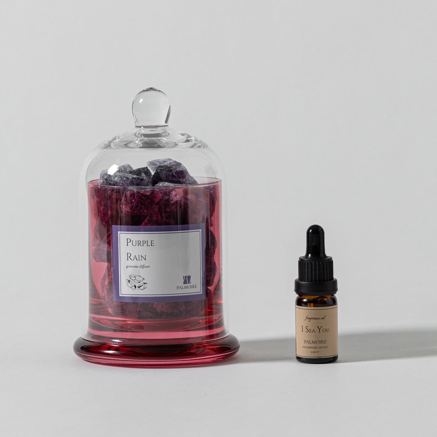 Glass jar labeled 'Purple Rain' with a dropper bottle on a light gray background