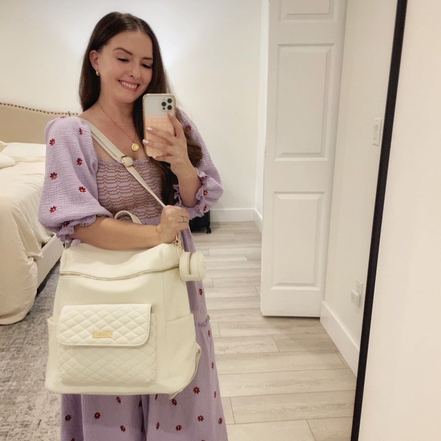 Woman holding a white quilted bag in a room with a bed and door in the background