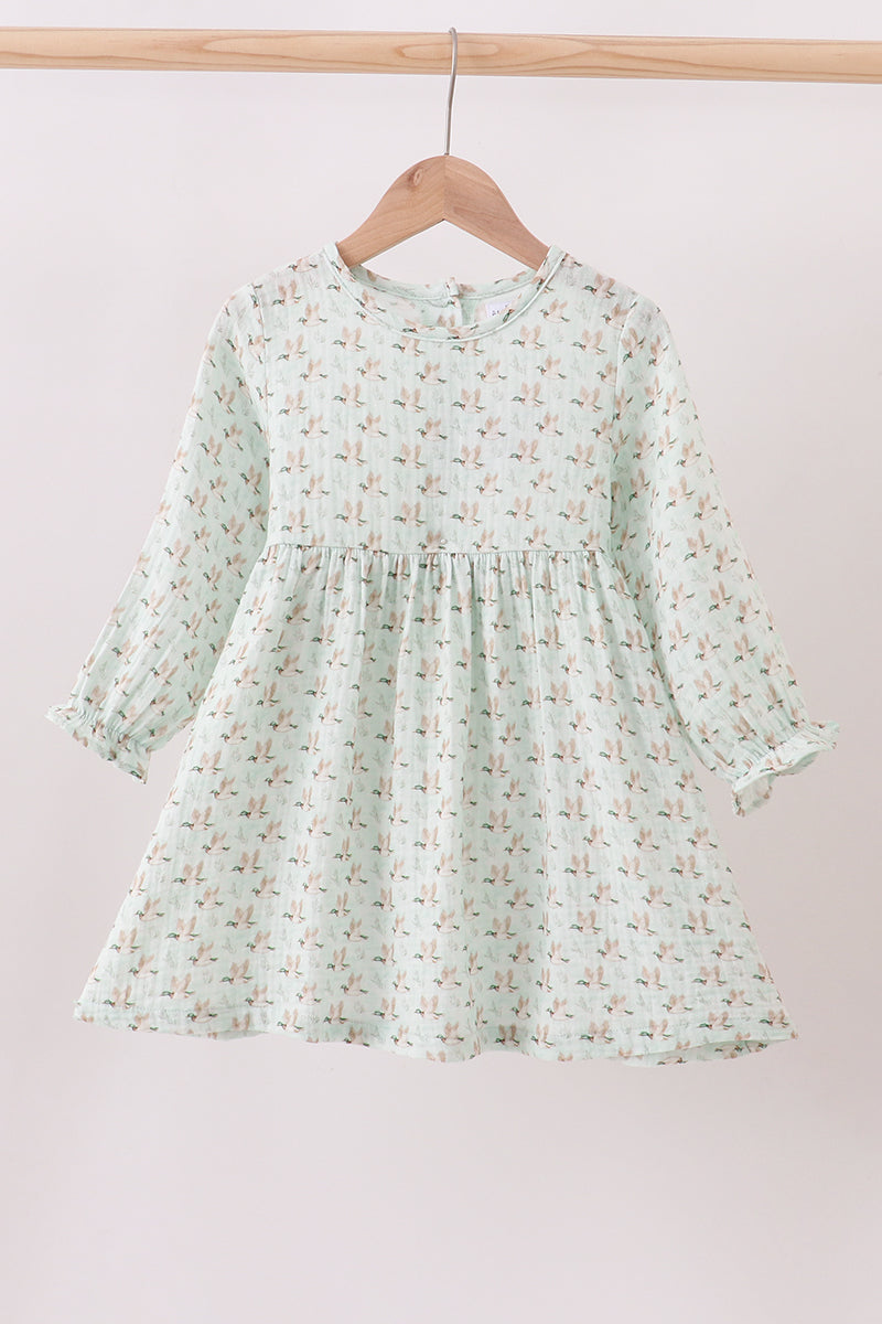 Light green floral dress on a wooden hanger against a light pink background