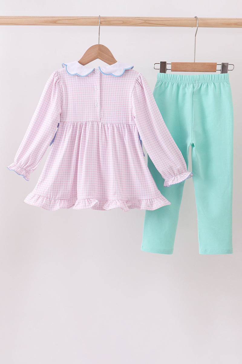 Pink checkered dress with white collar and green leggings on hangers against a light gray background