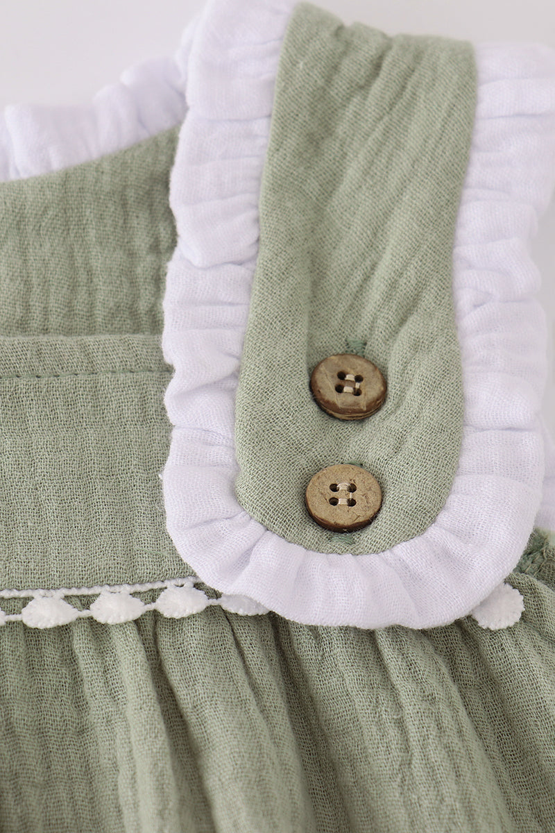 Green fabric with white ruffle and wooden buttons on a light background