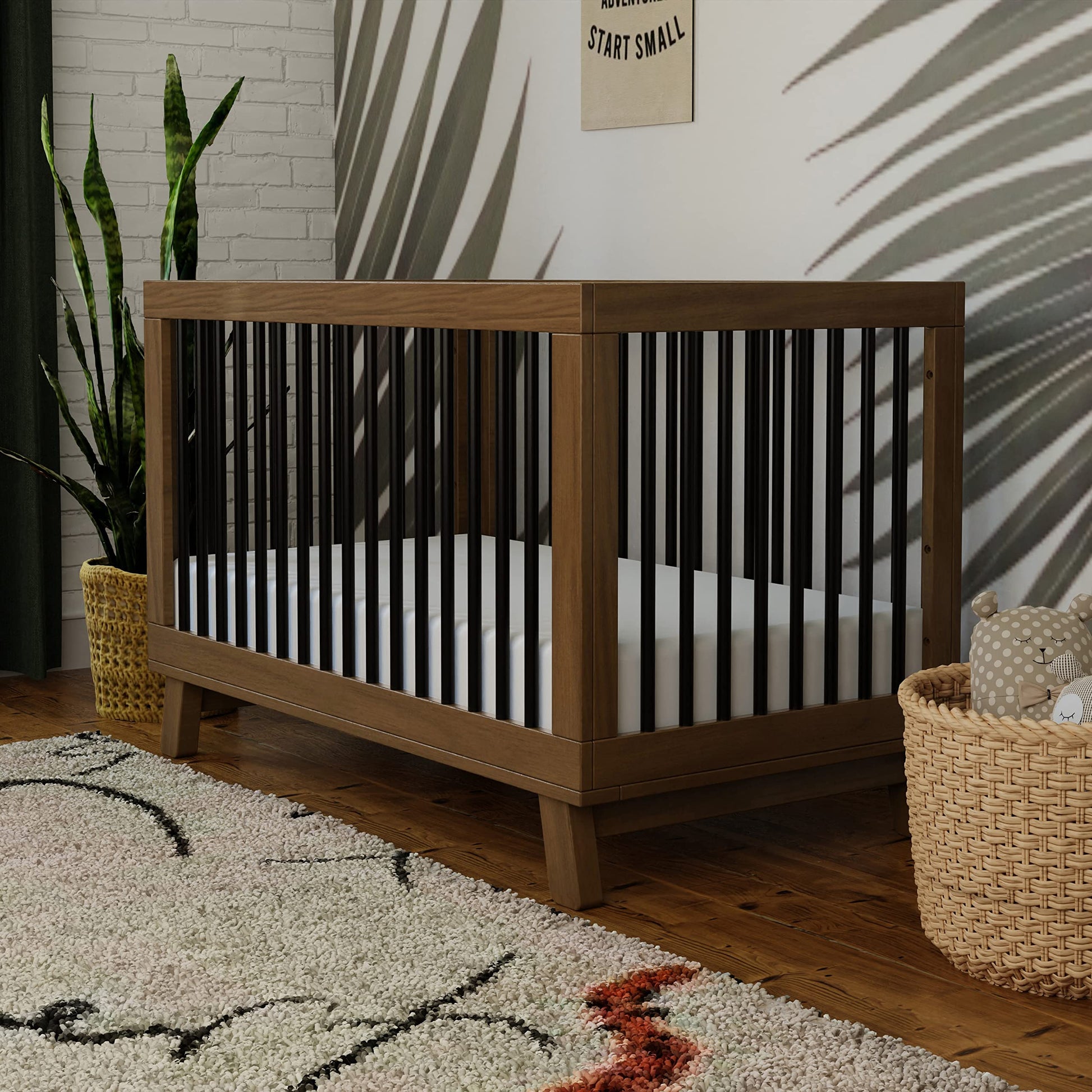 Wooden crib with black and white striped bedding in a room with a plant and rug.