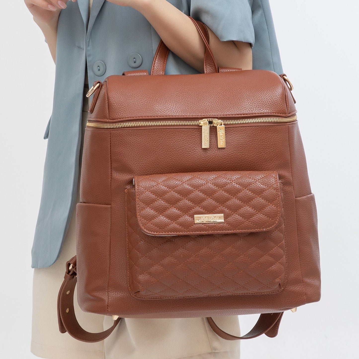 Brown leather backpack with a quilted pocket held by a person wearing a light blue jacket.
