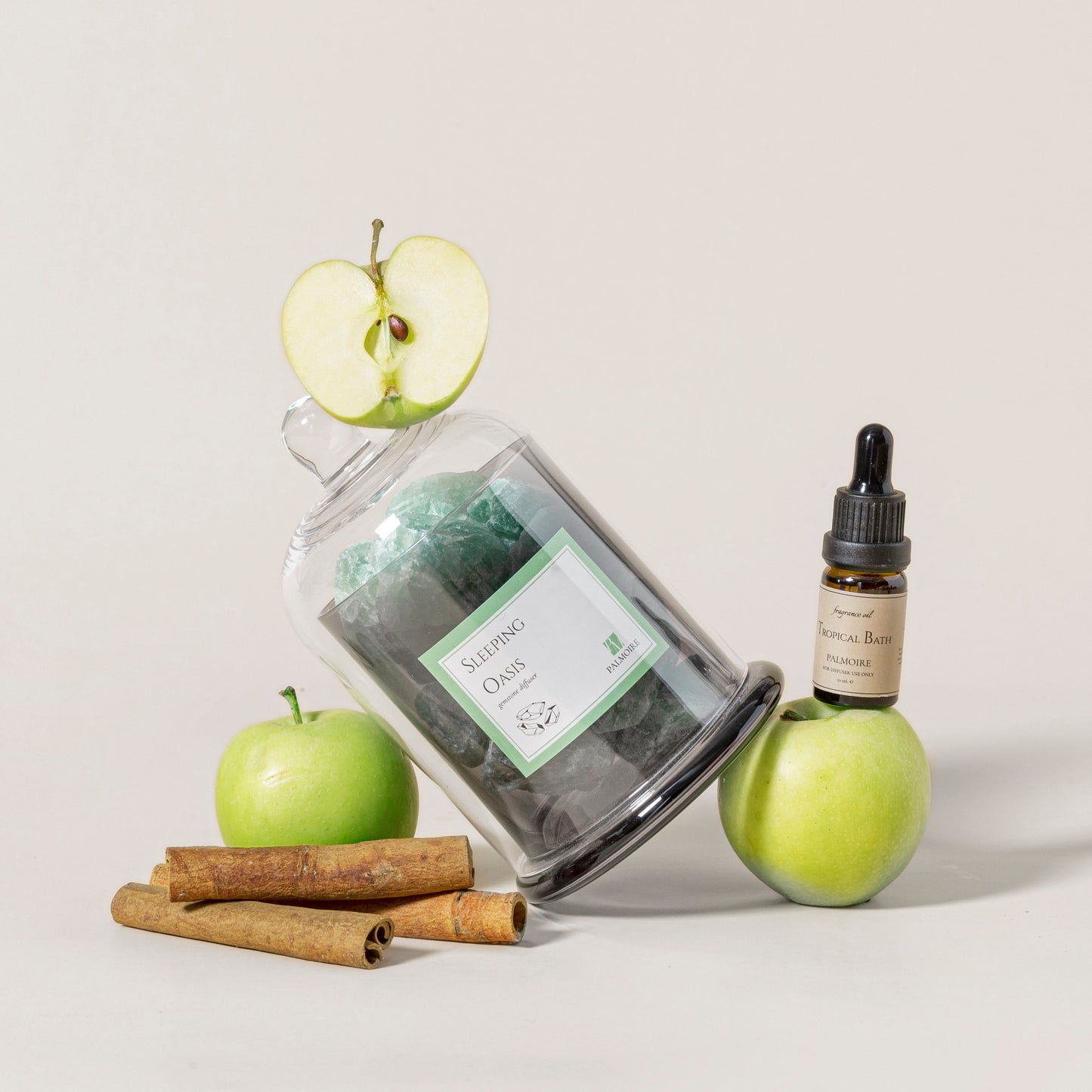 Jar of green tea, apple, cinnamon sticks, and a bottle with dropper on a light background