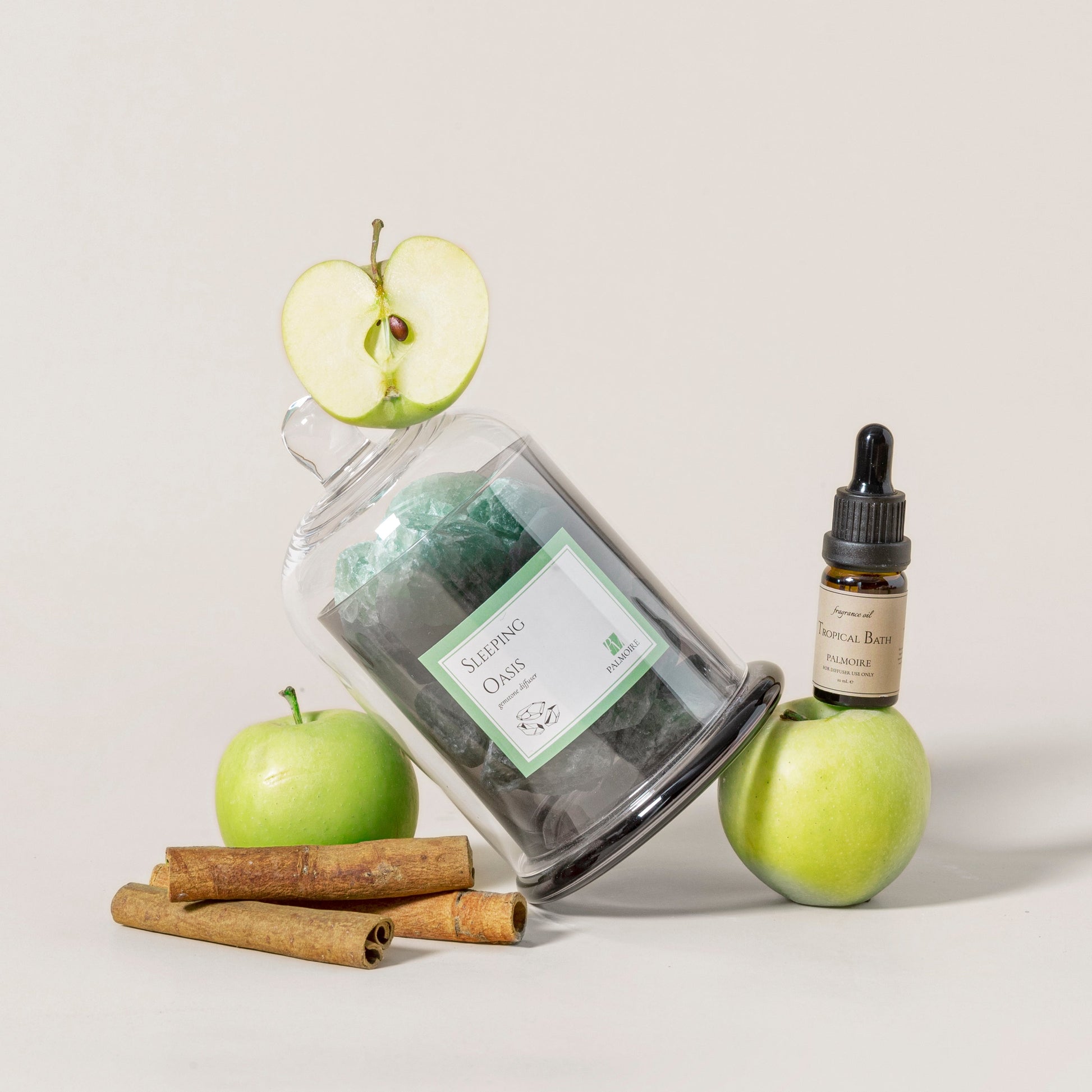 Jar of green tea, apple, cinnamon sticks, and a bottle with dropper on a light background