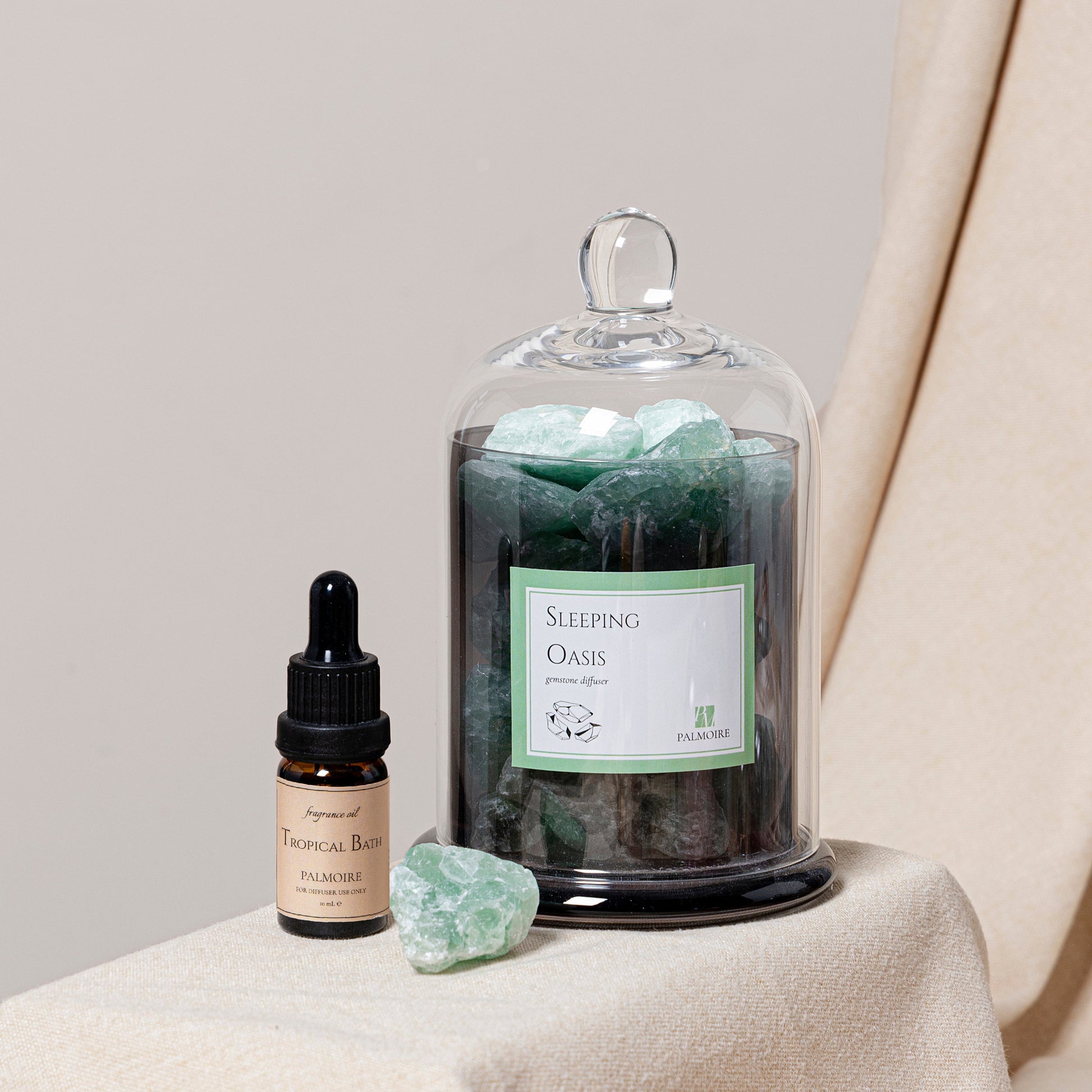 A bottle of 'Sleeping Oasis' with a dropper and a glass container with green crystals on a beige surface.