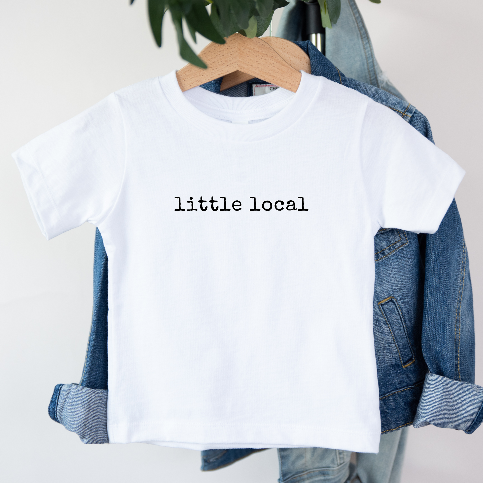 White t-shirt with 'little local' text on a hanger with denim jacket