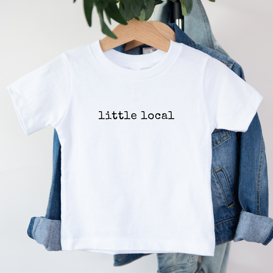 White t-shirt with 'little local' text on a hanger with denim jacket