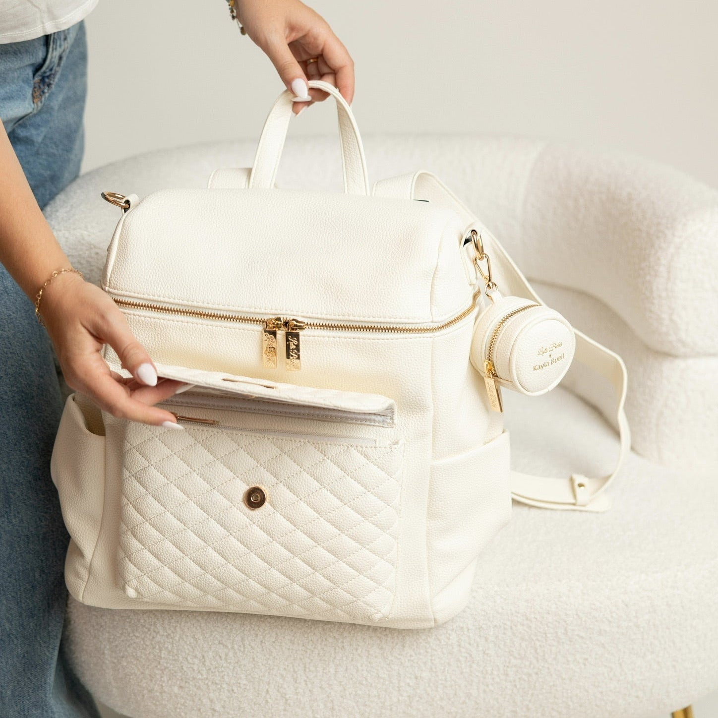White quilted handbag with gold accents held by a person on a light gray background
