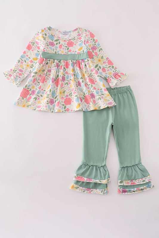 Children's outfit with floral top and green ruffled pants on a light gray background