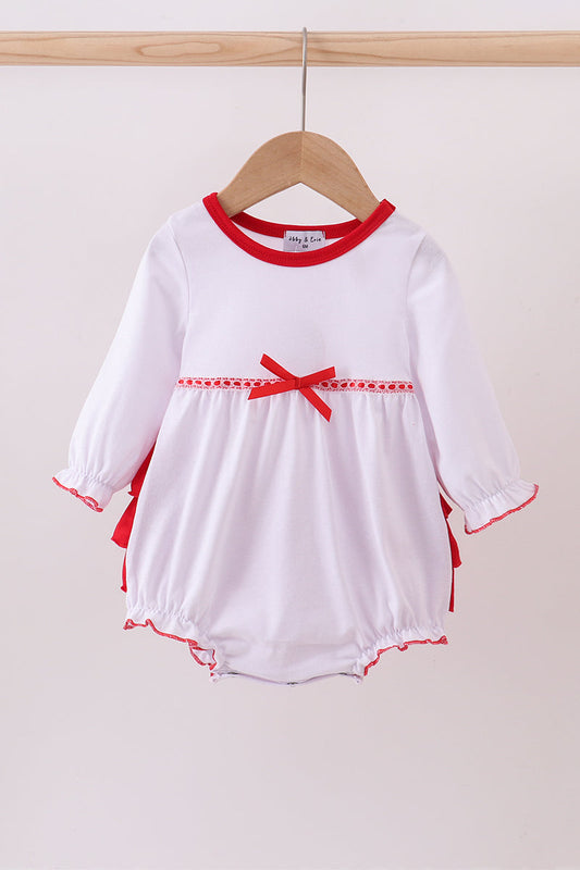 White baby romper with red trim and bow on a wooden hanger against a white background
