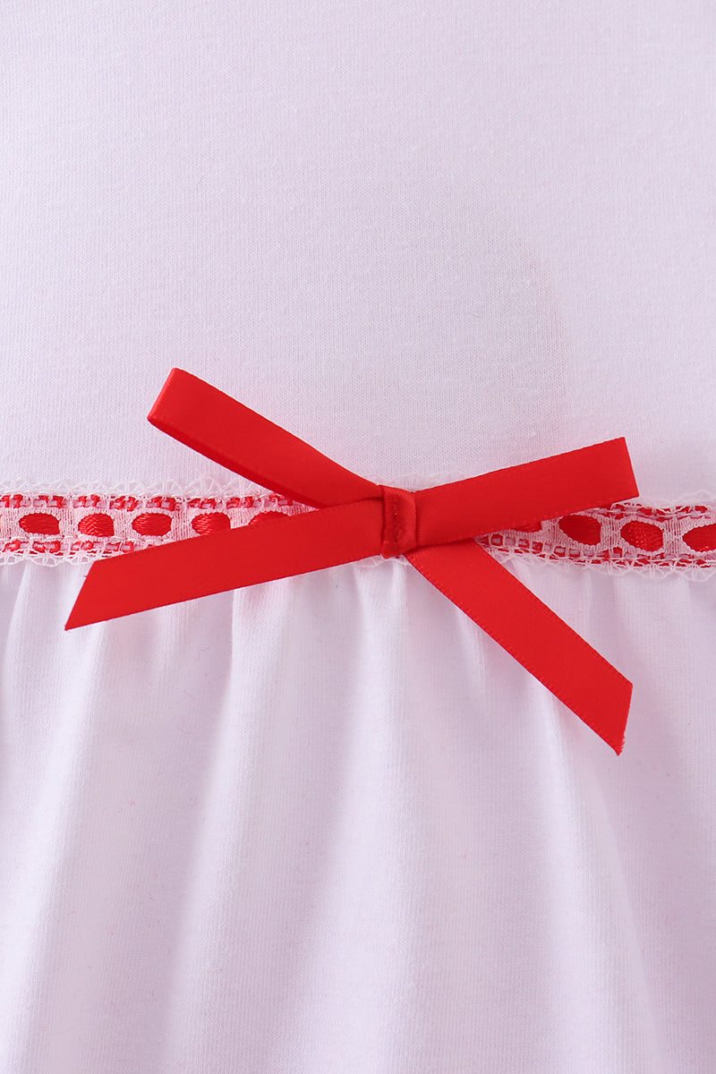 Red bow on a white dress with lace trim