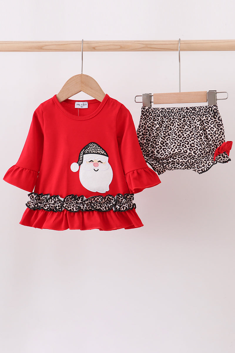 Red dress with Santa Claus design and leopard print trim, paired with leopard print shorts on a wooden rack.