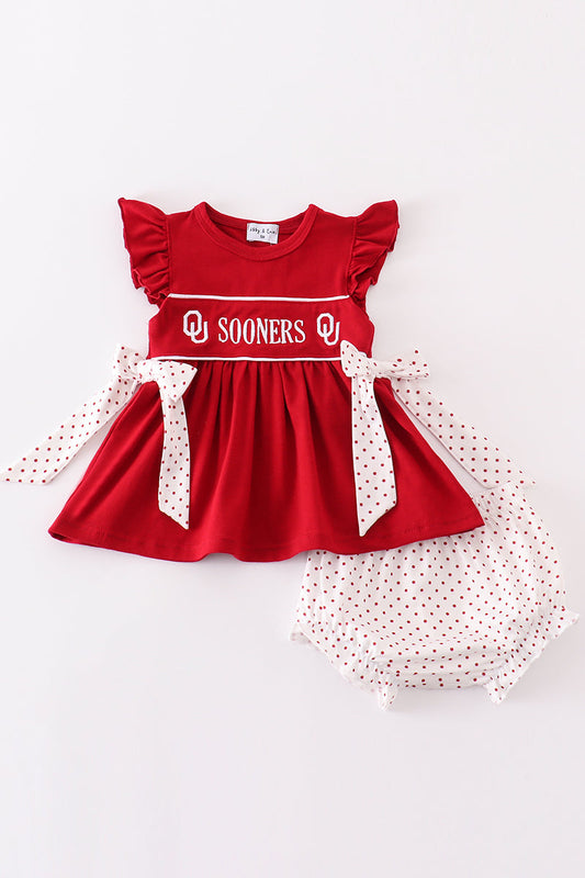 A set of children's clothing, with a red top that has 'SOONERS' written on it in white letters, and white bloomers with a polka dot pattern.
