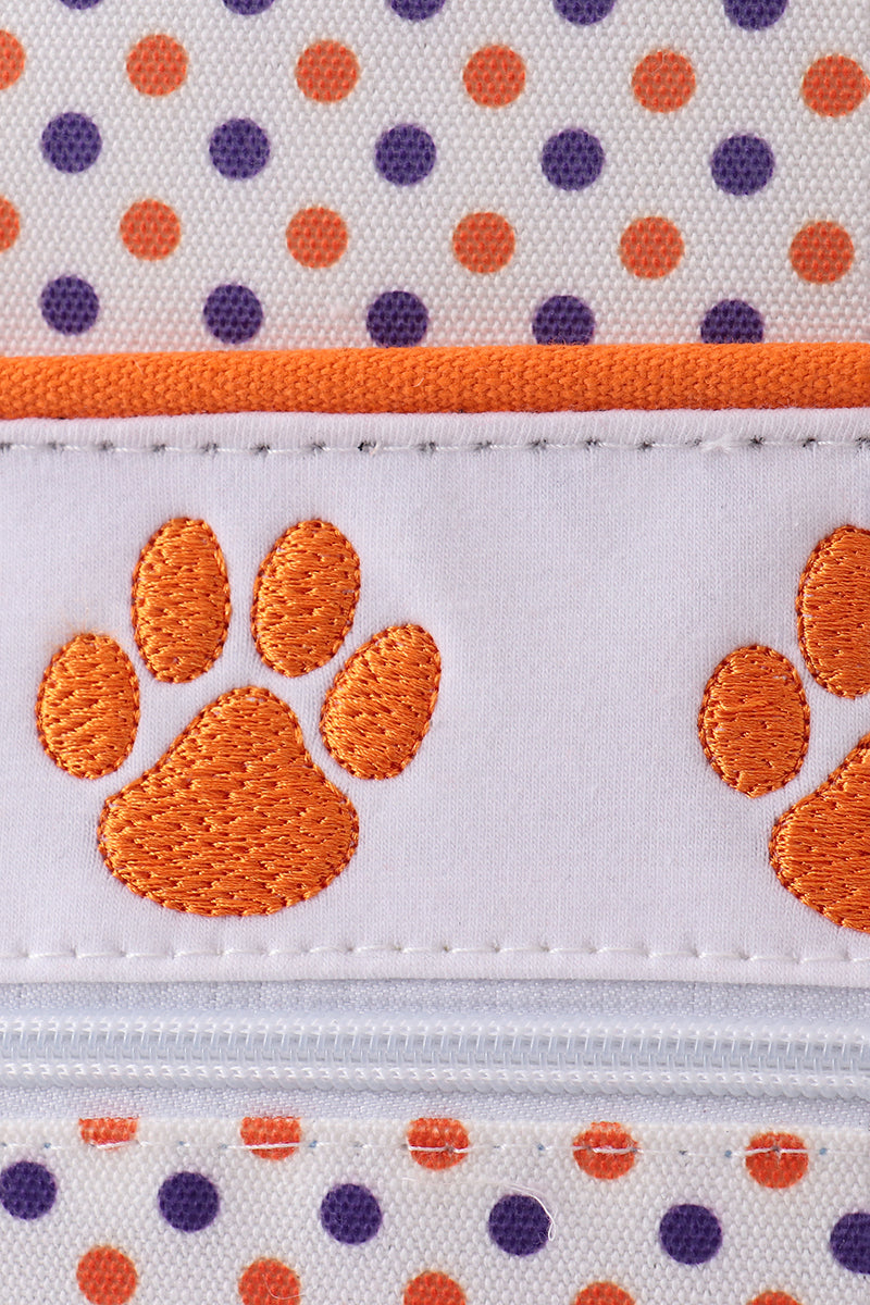 Close-up of fabric with orange paw prints and polka dots.