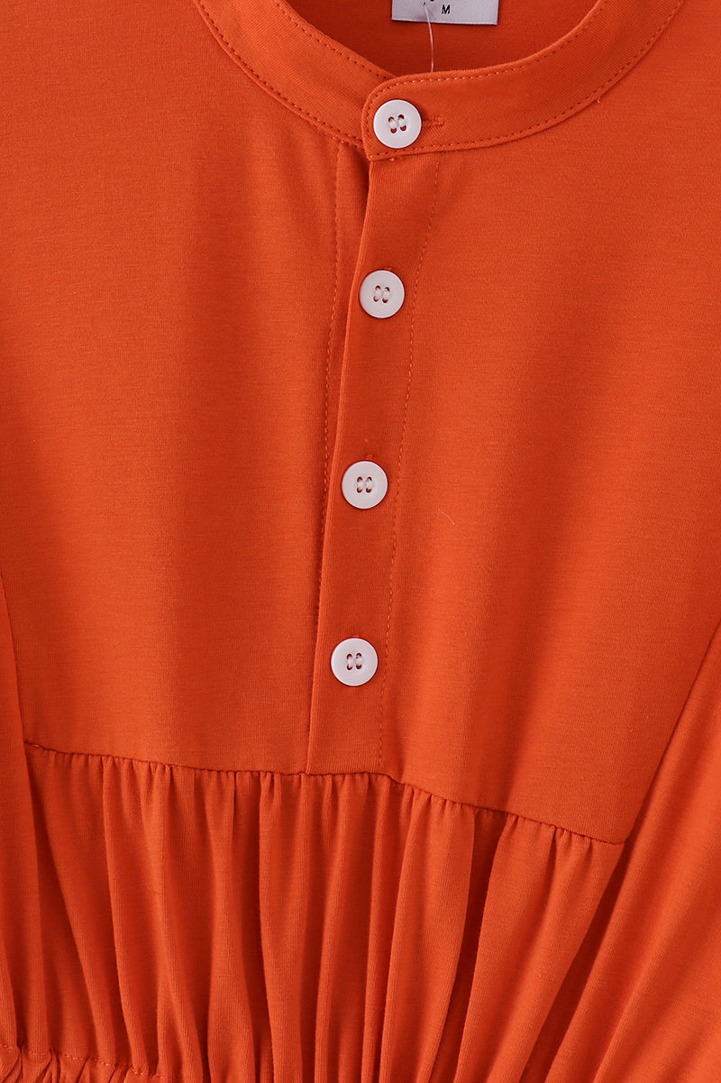 Close-up of an orange dress with buttons on a plain background