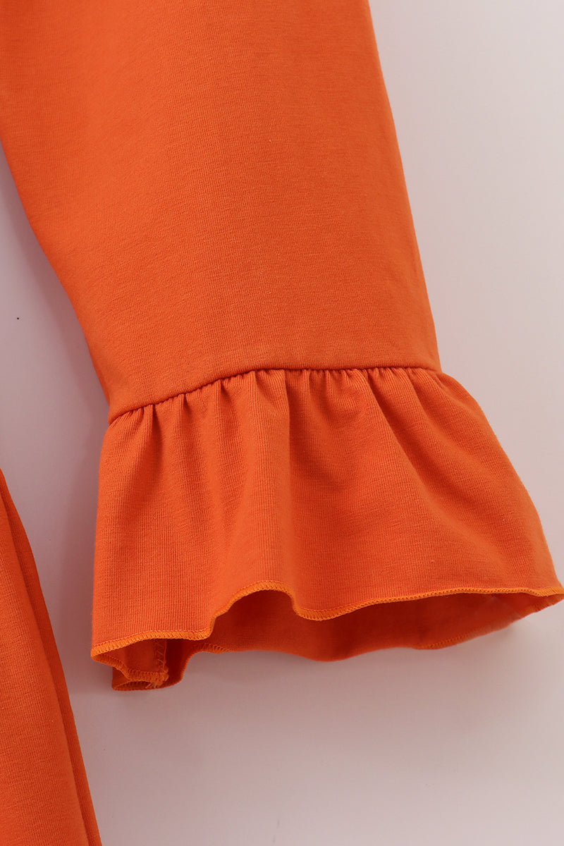 Close-up of orange pants with ruffled hem on a light pink background