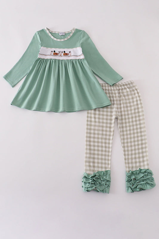 Green dress with floral embroidery and checkered pants on a white background