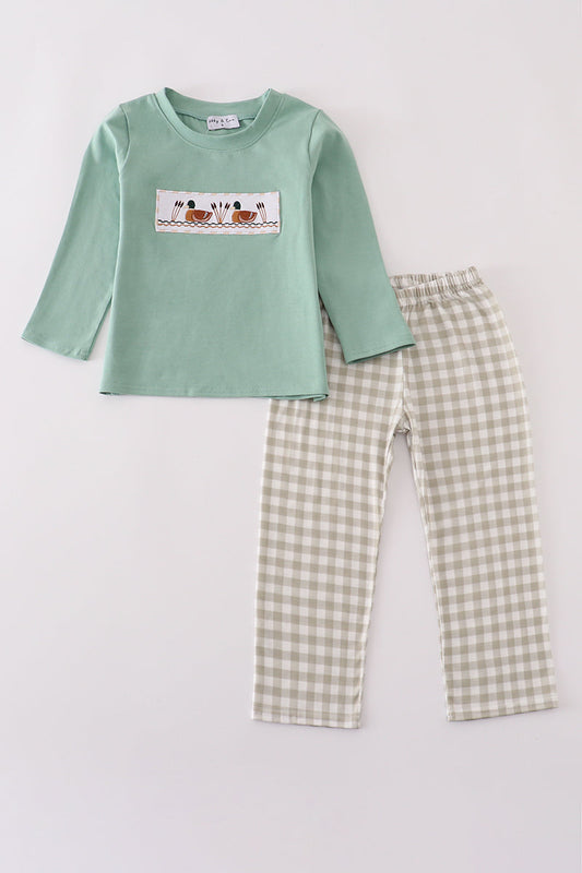 Children's green long-sleeve shirt with a graphic and checkered pants on a light gray background