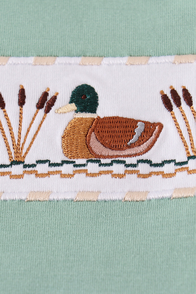 Embroidered design of a duck and reeds on a fabric background