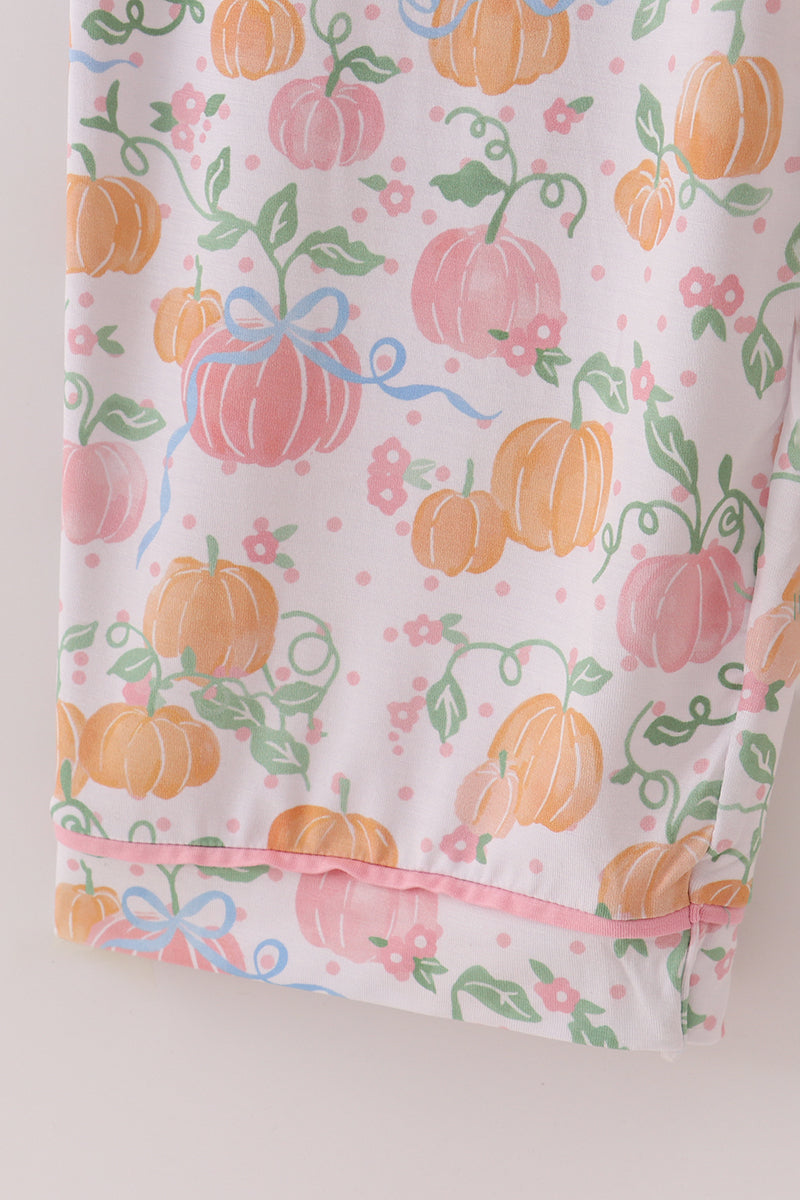Fabric with pumpkins, ribbons, and flowers on a light pink background
