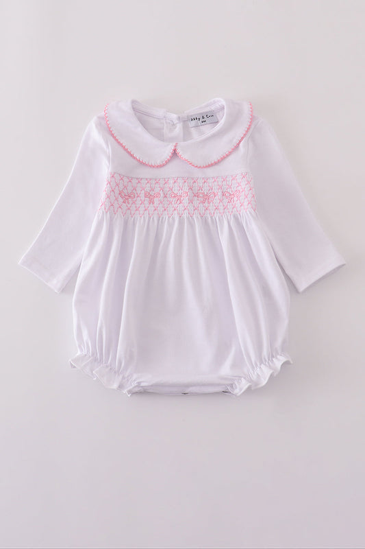 White baby romper with pink smocking on a light gray background