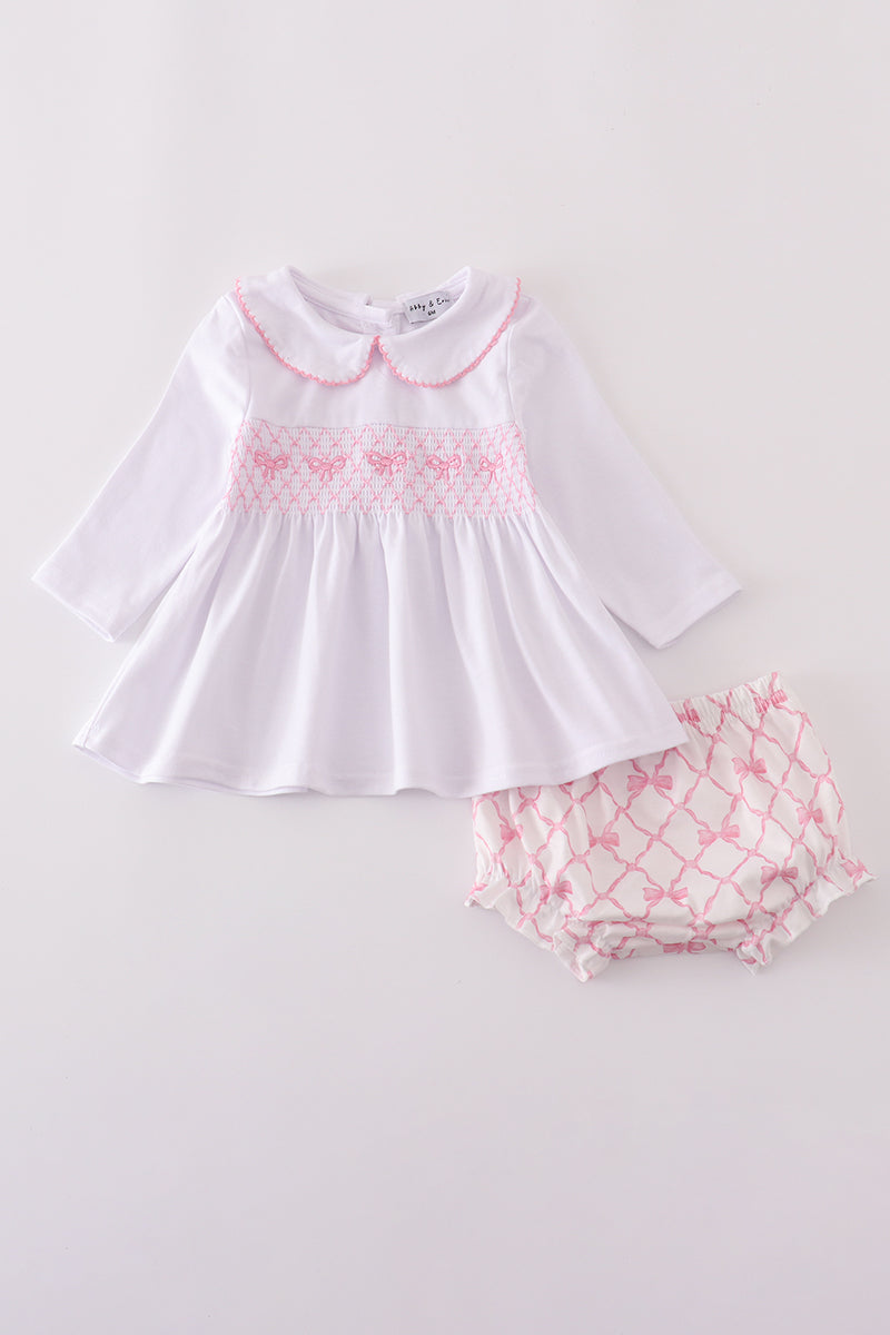 White dress with pink smocking and matching bloomers on a light gray background