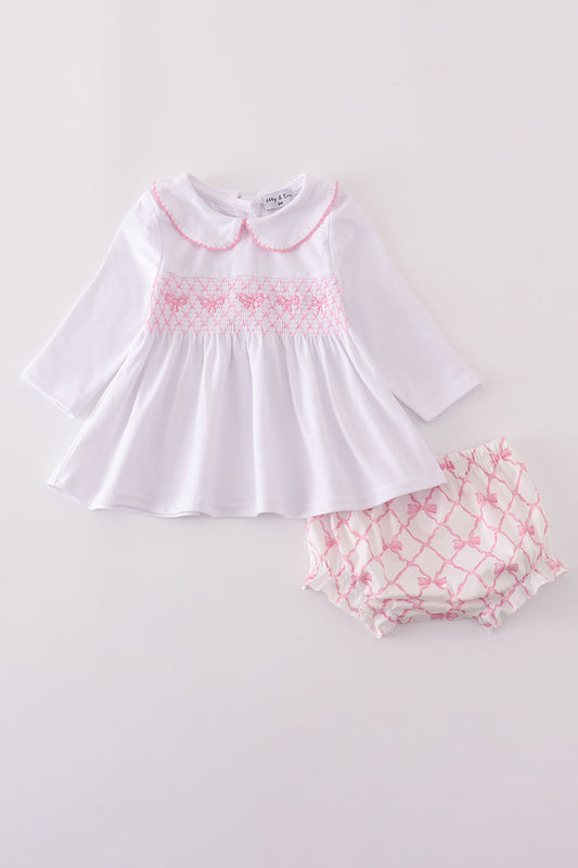 White dress with pink smocking and matching bloomers on a light gray background