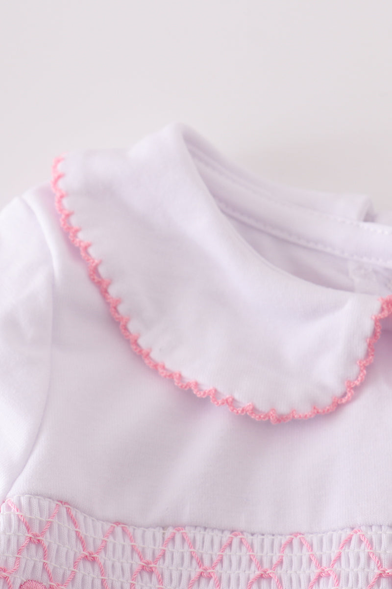 Close-up of a white garment with pink embroidery on a light background