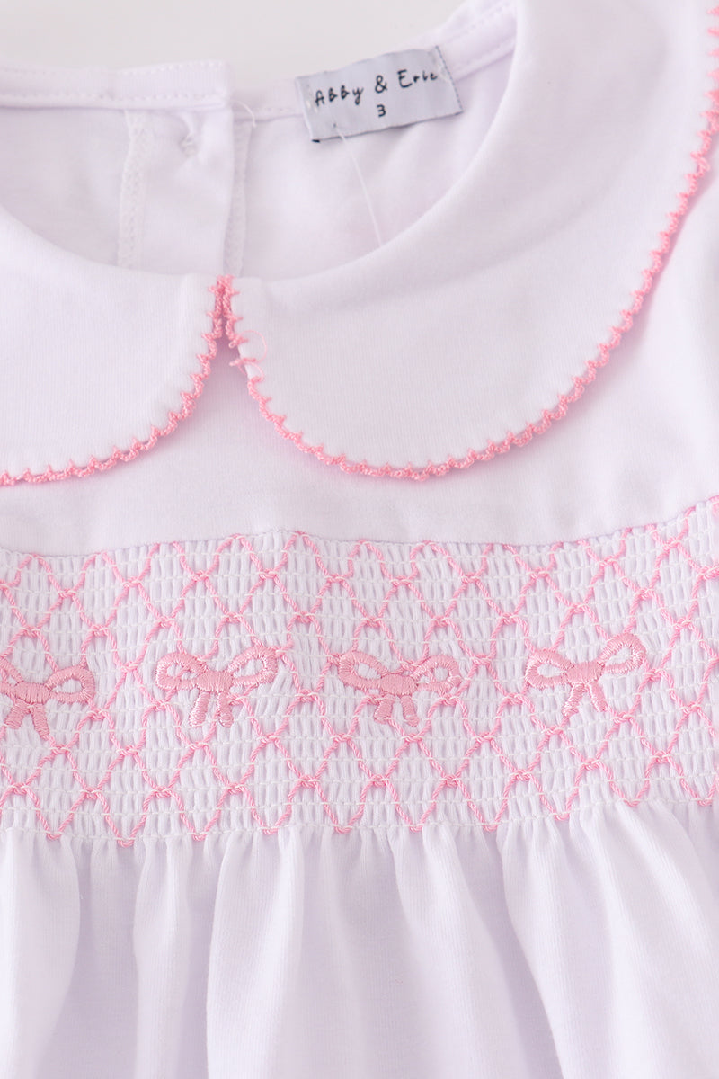 White dress with pink smocked collar and hem, brand label visible.