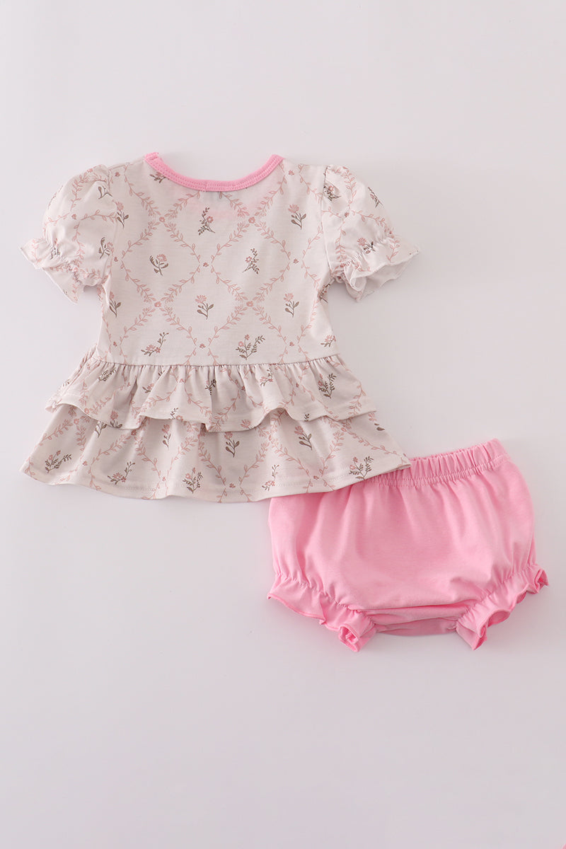 Baby outfit with a ruffled top and pink bloomers on a light gray background