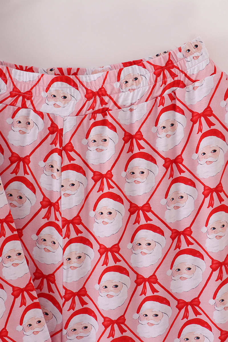 Patterned fabric with Santa Claus faces and red bows on a pink background