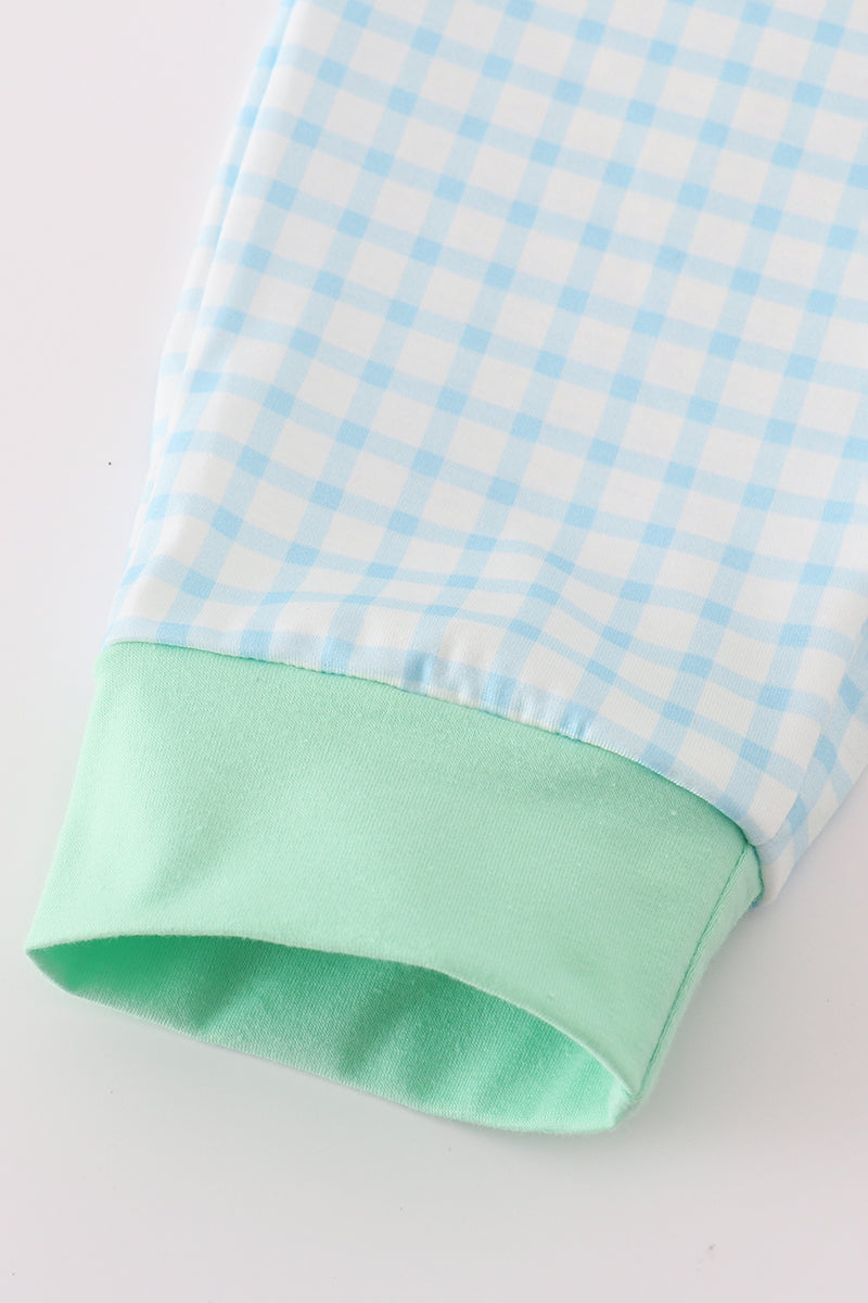 Close-up of a fabric with blue and white checkered pattern and green trim on a light gray background
