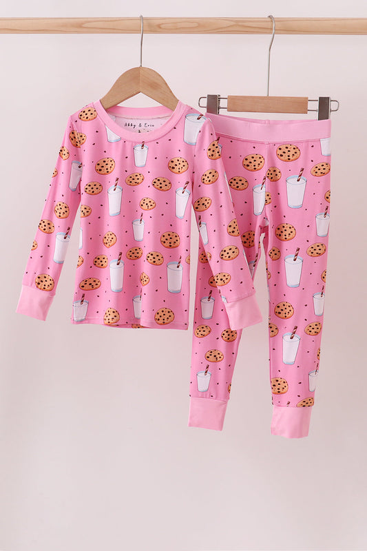 Pink children's pajama set with animal and cookie pattern on a hanger against a pink background.