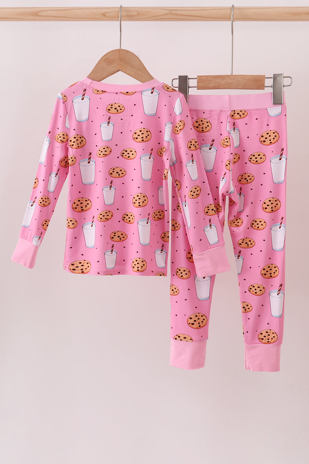 Pink pajama set with cookies and milk pattern on a hanger against a white background