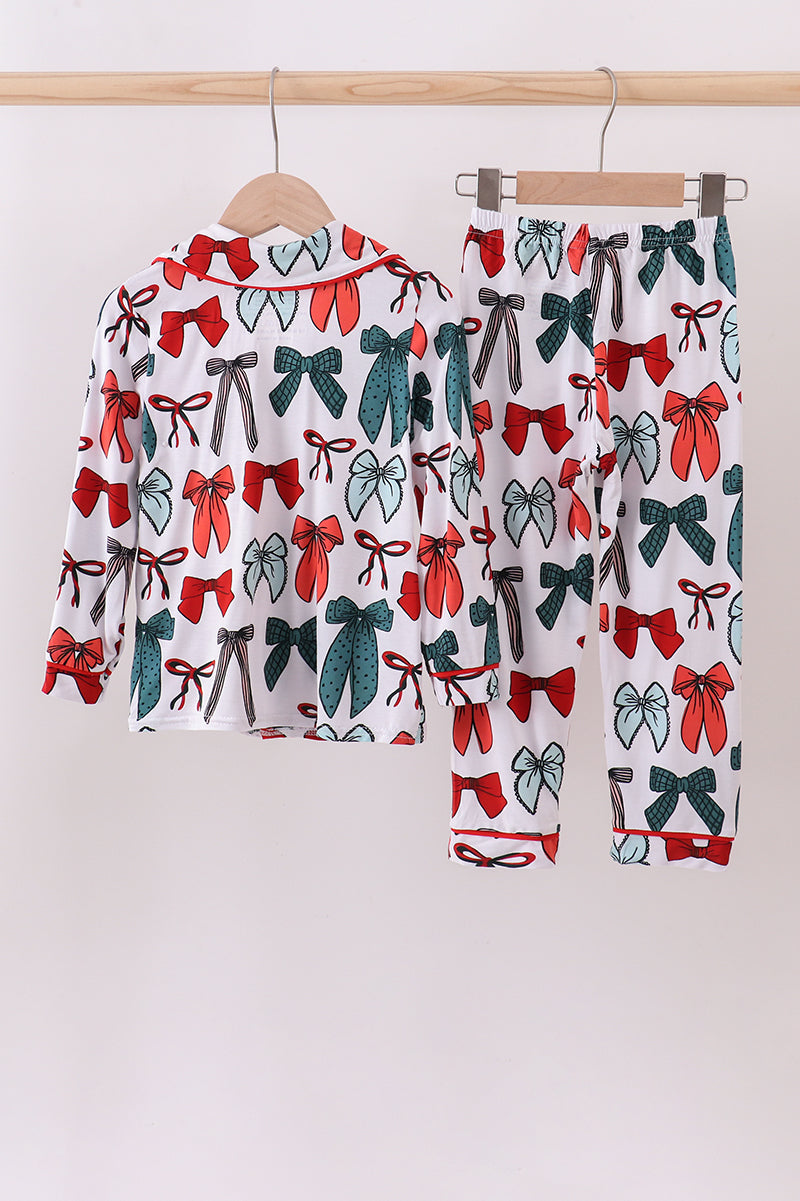 Children's pajama set with bow pattern on a wooden hanger against a white background