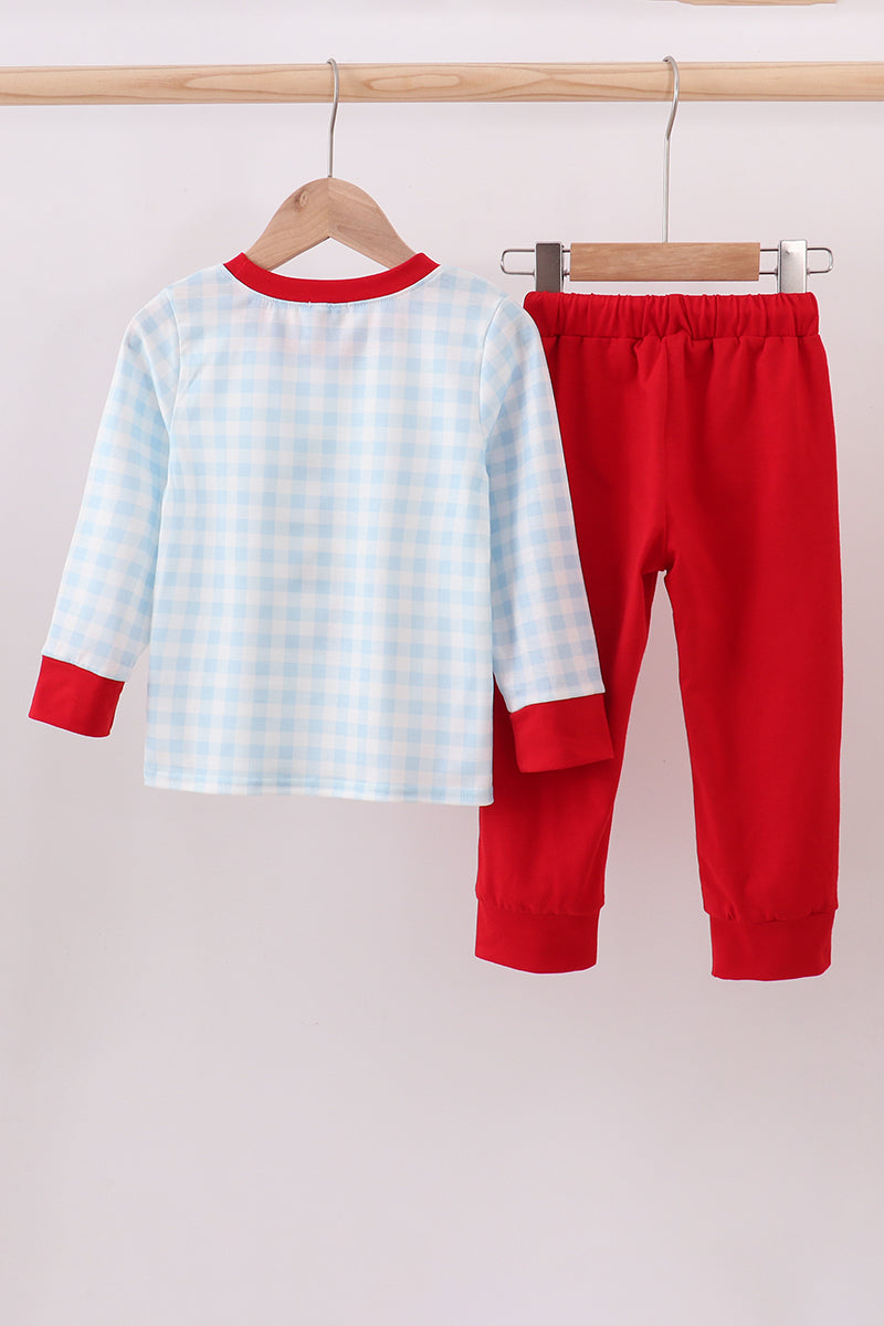 Children's outfit with checkered shirt and red pants on hangers against a white background