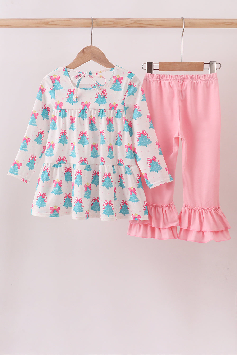 Children's outfit with a dress and pink pants on hangers against a light background