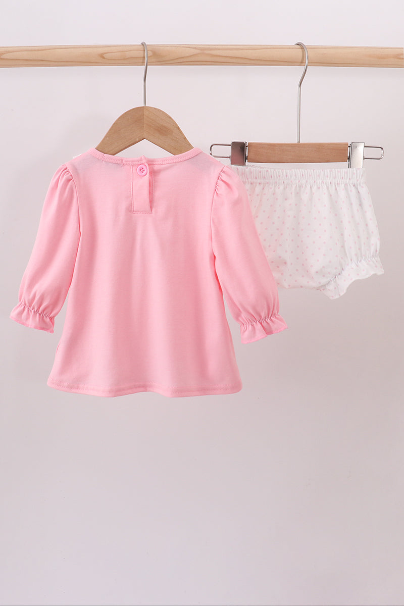 Pink long-sleeve top and white shorts on hangers against a light gray background