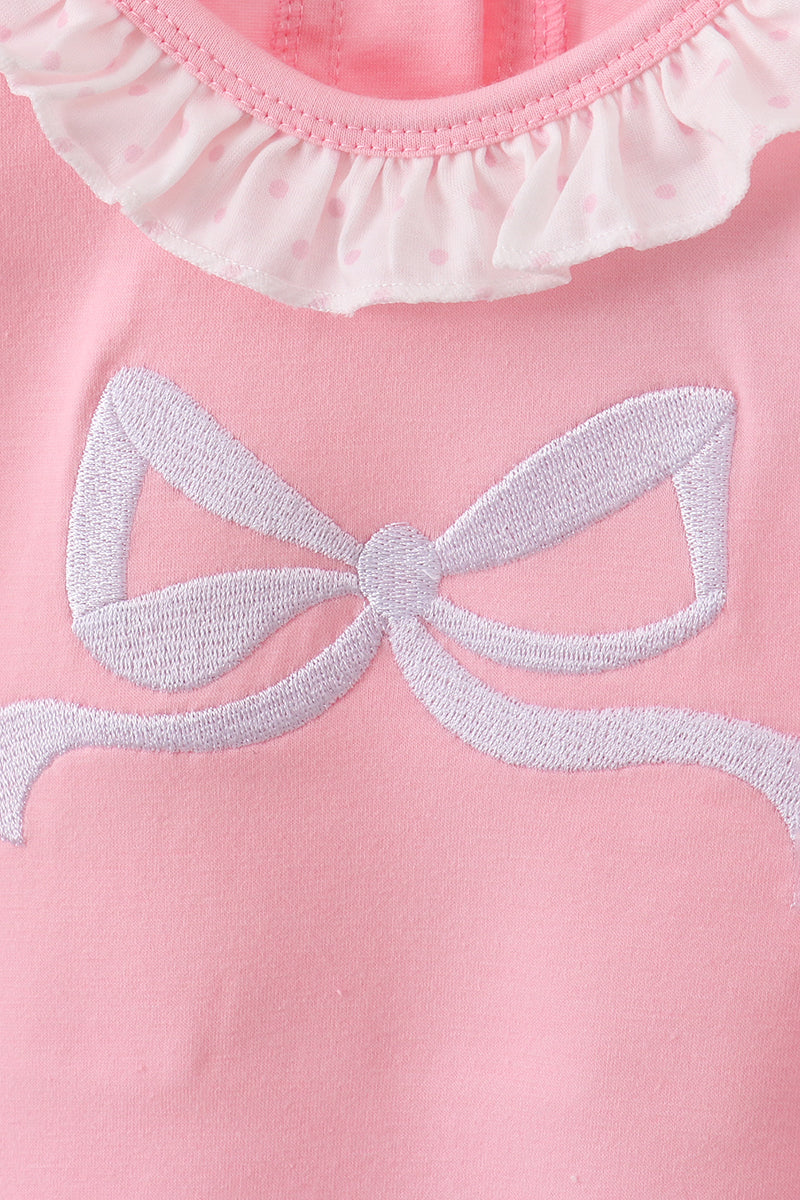 Close-up of a pink garment with a white embroidered bow detail.