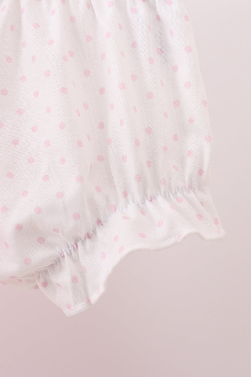 White baby romper with pink polka dots on a light pink background