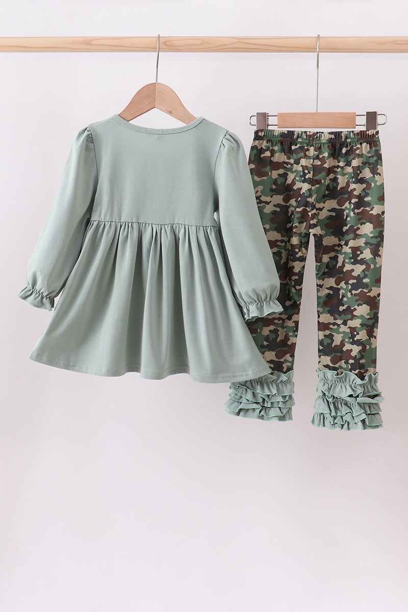 Children's outfit with green dress and camouflage pants on hangers against a white background