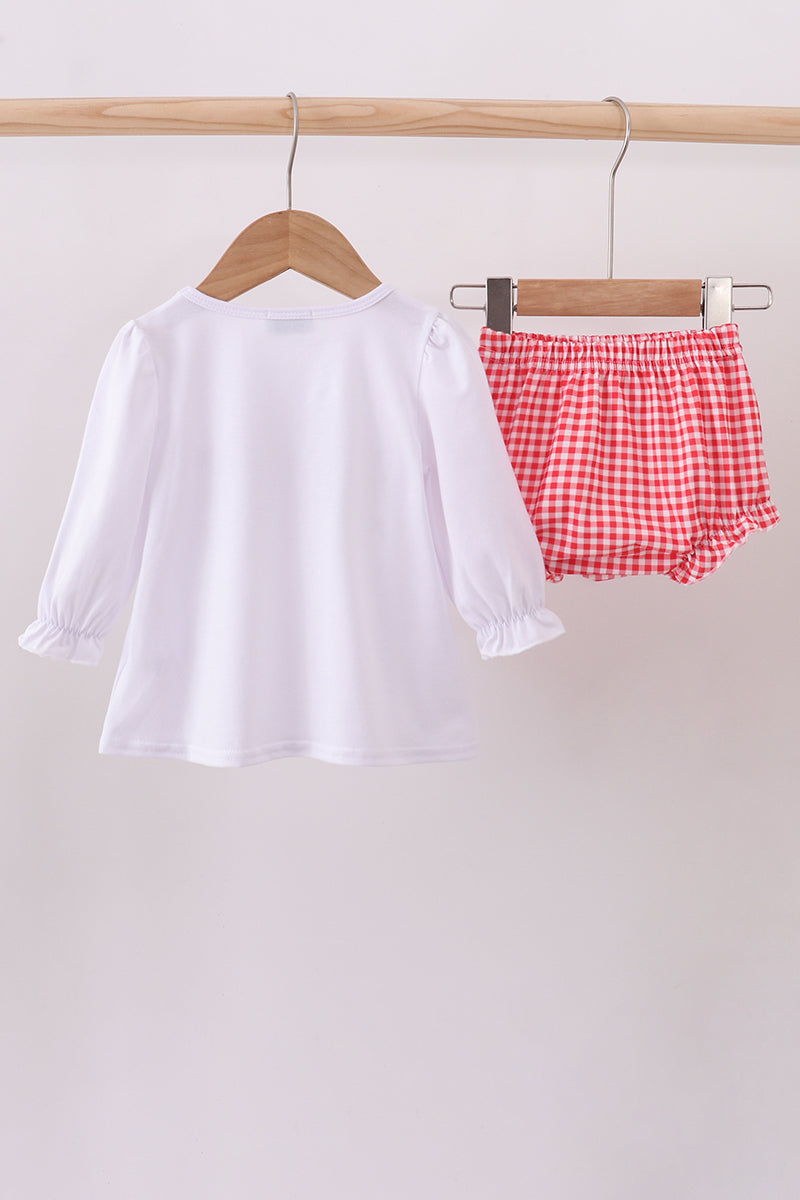 White long-sleeve shirt and red checkered shorts hanging on a wooden rack against a white background.