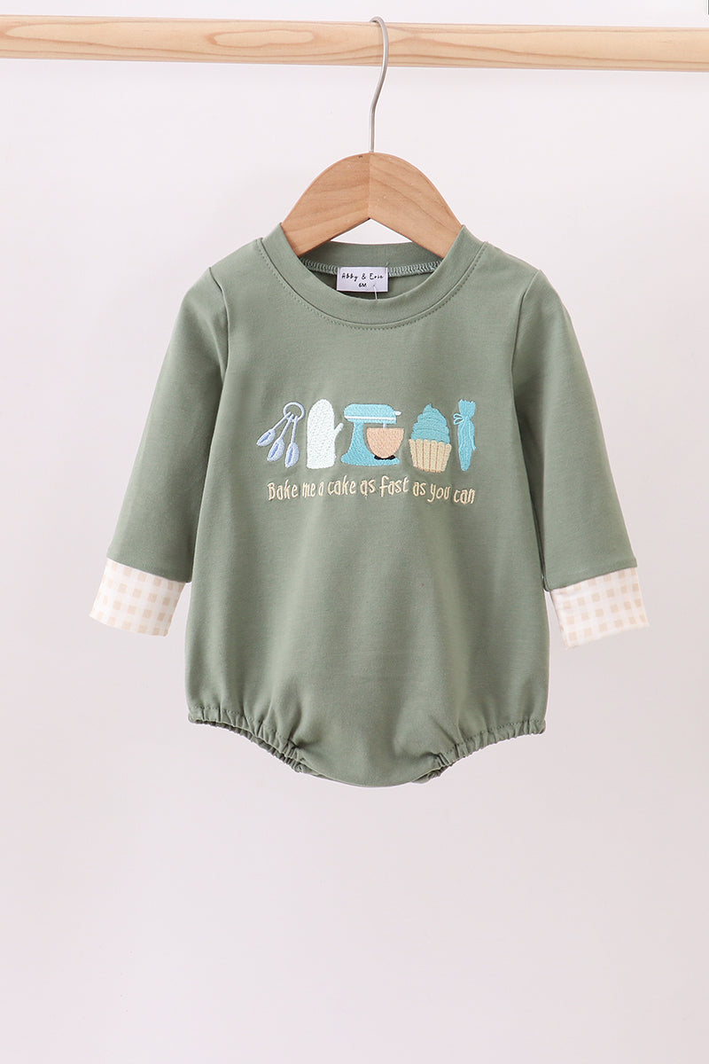 Green baby romper with printed design on a wooden hanger against a light background